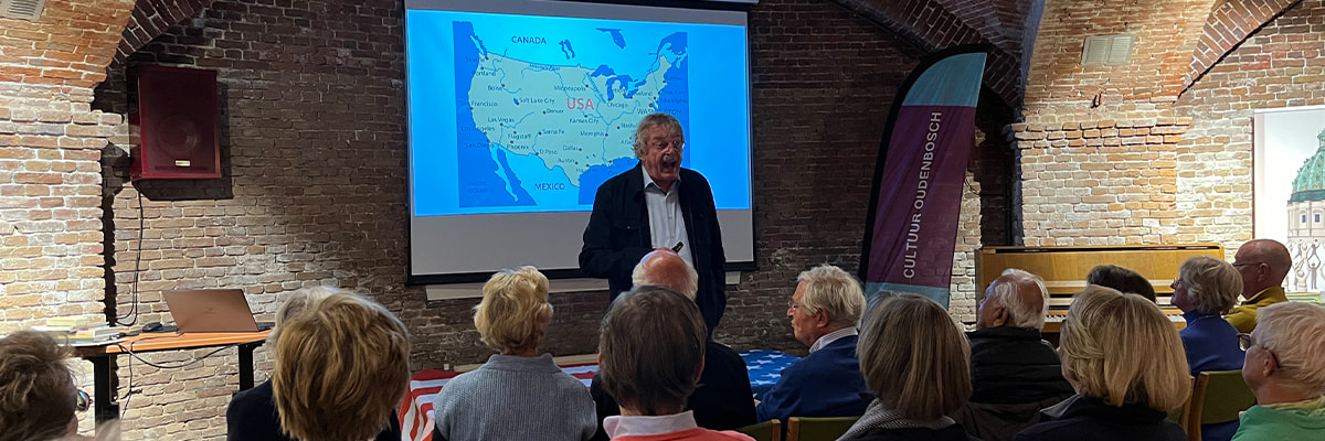 persoon geeft een presentatie voor een groot scherm tenover een volle zaal luisteraars